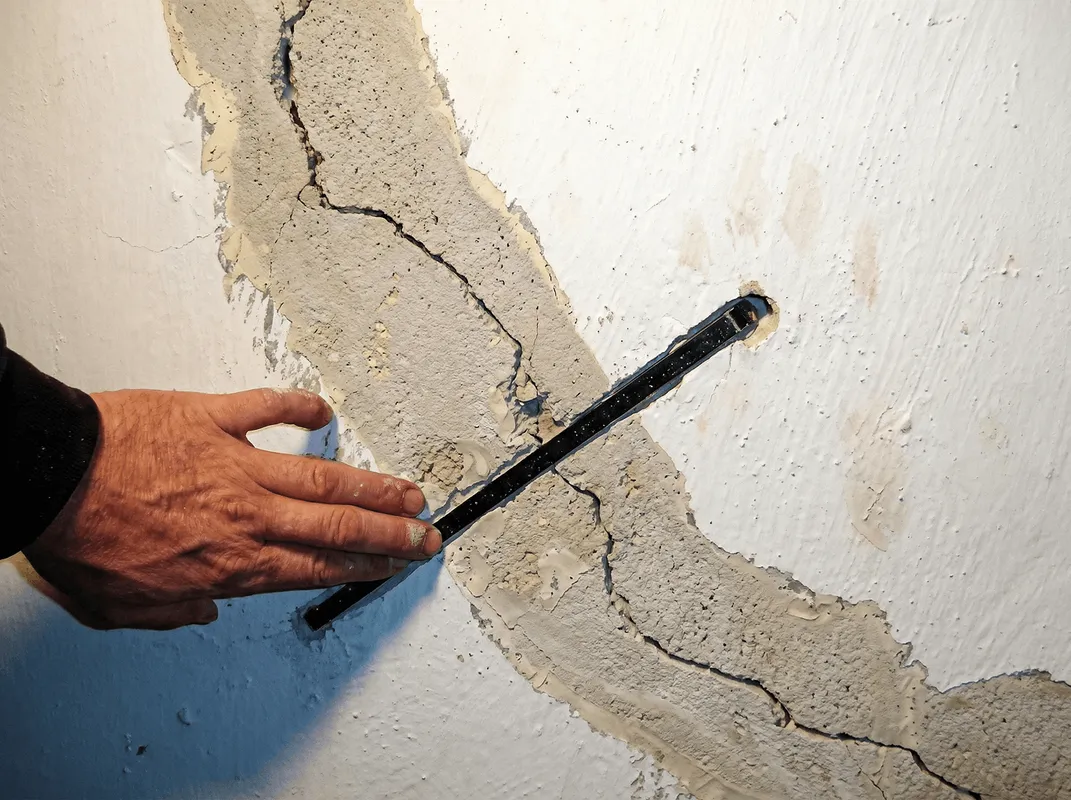 A wall with a large crack is being inspected by a professional in Cambridge, MA